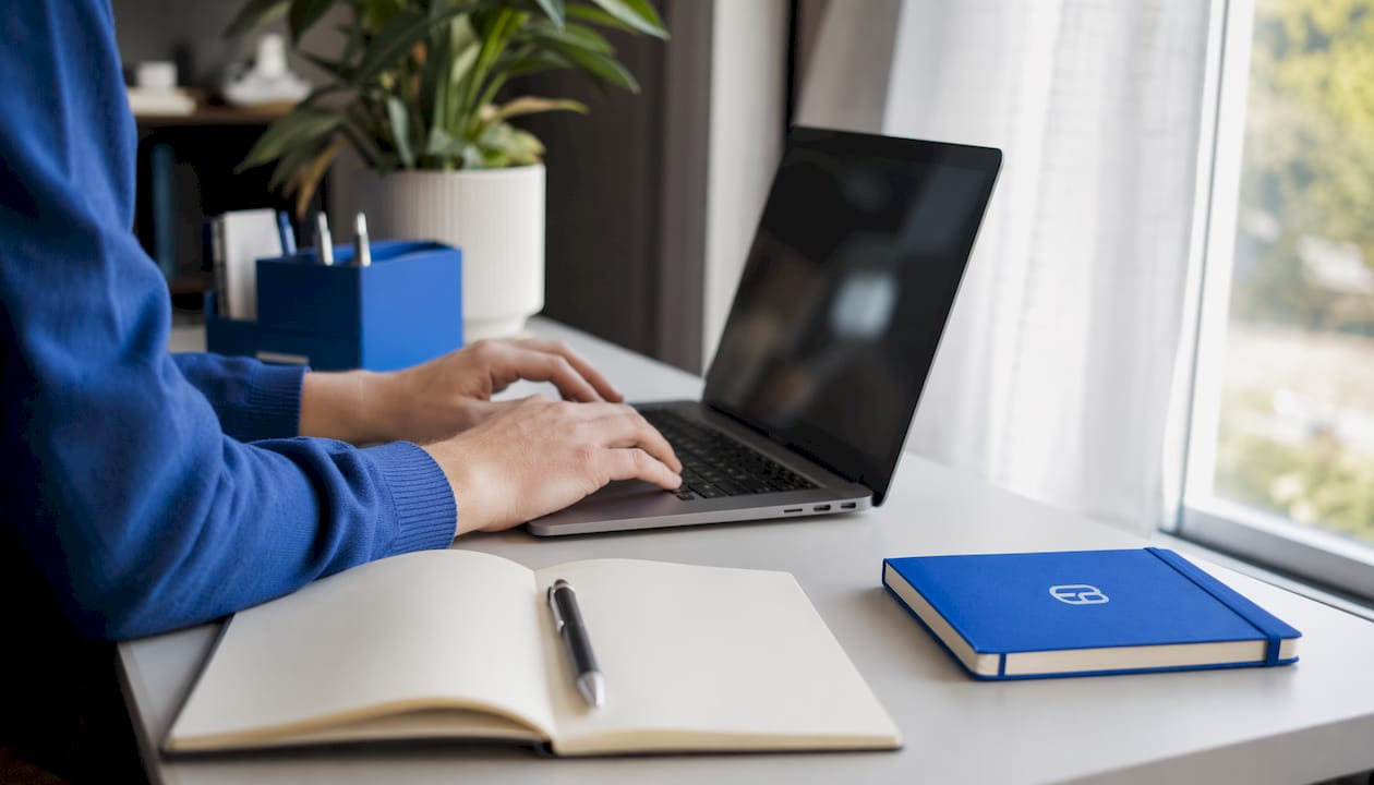 Hands typing on laptop with accounting papers